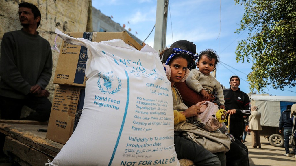Family seated on cart with bag of grain