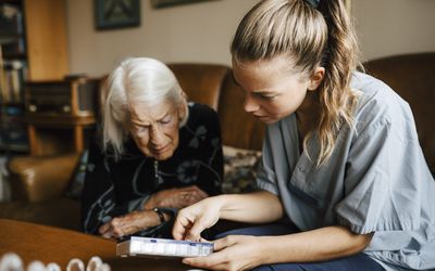 Female healthcare provider explaining medicine dose to older female at home