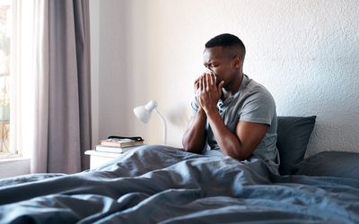 A man sitting in bed and blowing his nose from allergies or a cold