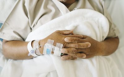 A person with an IV on their hand lying in a bed