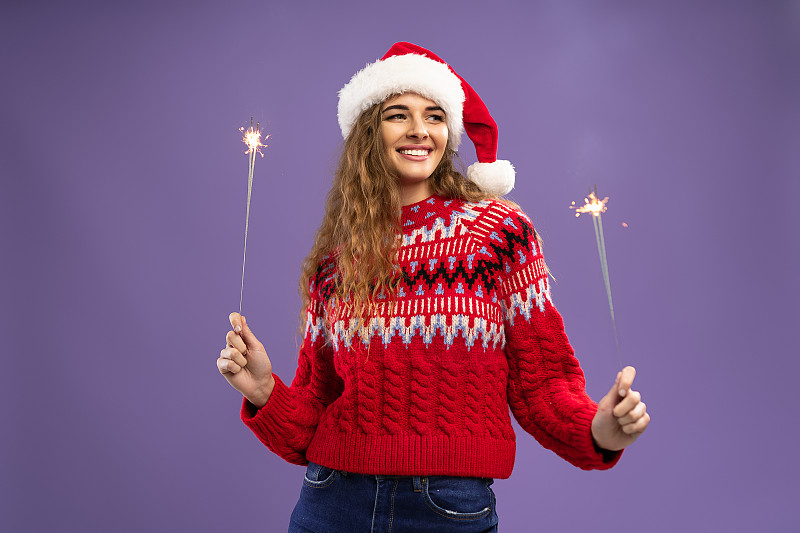 微笑的年轻女子戴着圣诞老人的帽子，在燃烧的烟花上跳舞图片下载