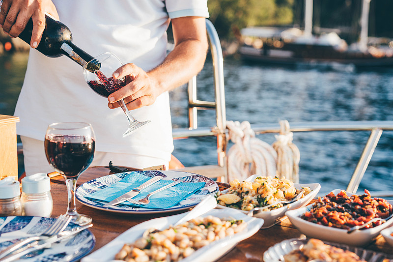朋友在日落时分的游艇上喝酒。人倒酒。图片下载