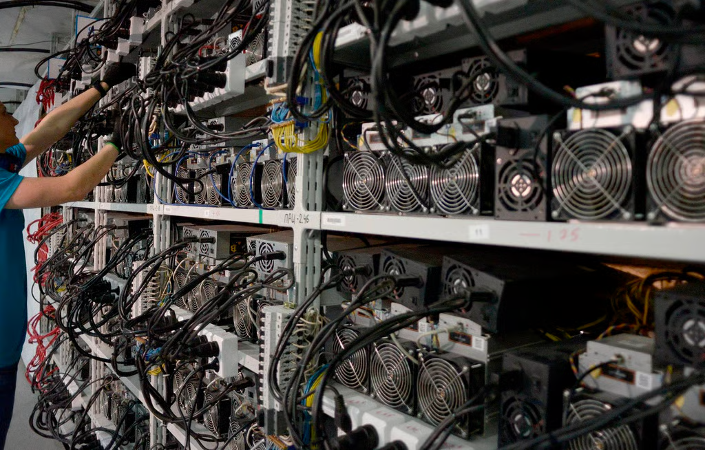 图为 2018 年,俄罗斯一家公司内,一名男子正在检查用于加密货币挖矿的机器。来源:法新社)