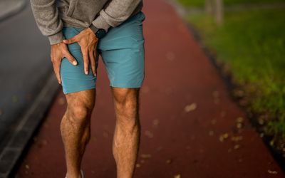 hip flexor pain; Hand close-up of young male athlete holding his injured leg during outdoor exercise.