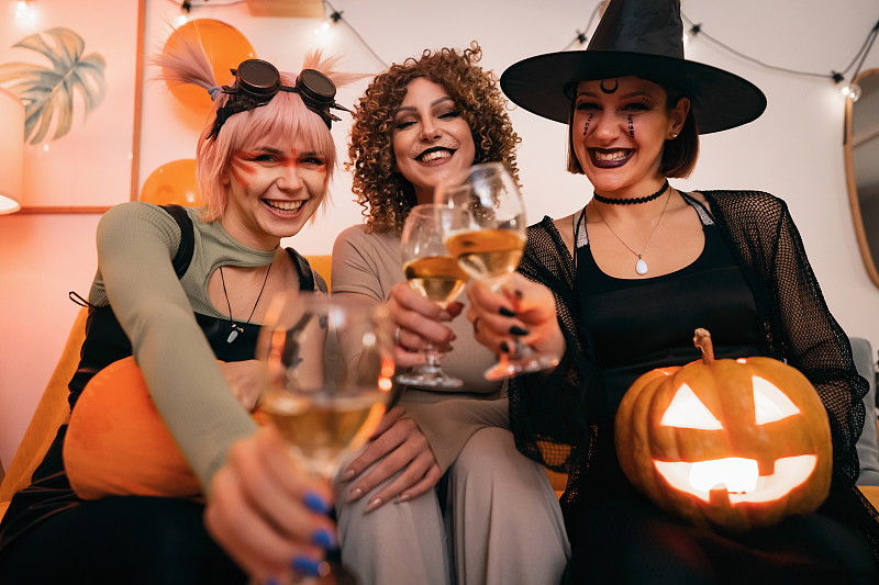 三个穿着万圣节服装的年轻白人女性一起喝着酒,玩得很开心图片下载
