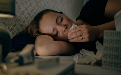 A person coughing into a tissue while lying in bed
