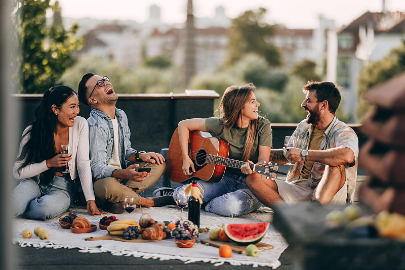 在屋顶上野餐时快乐的年轻朋友们。图片下载